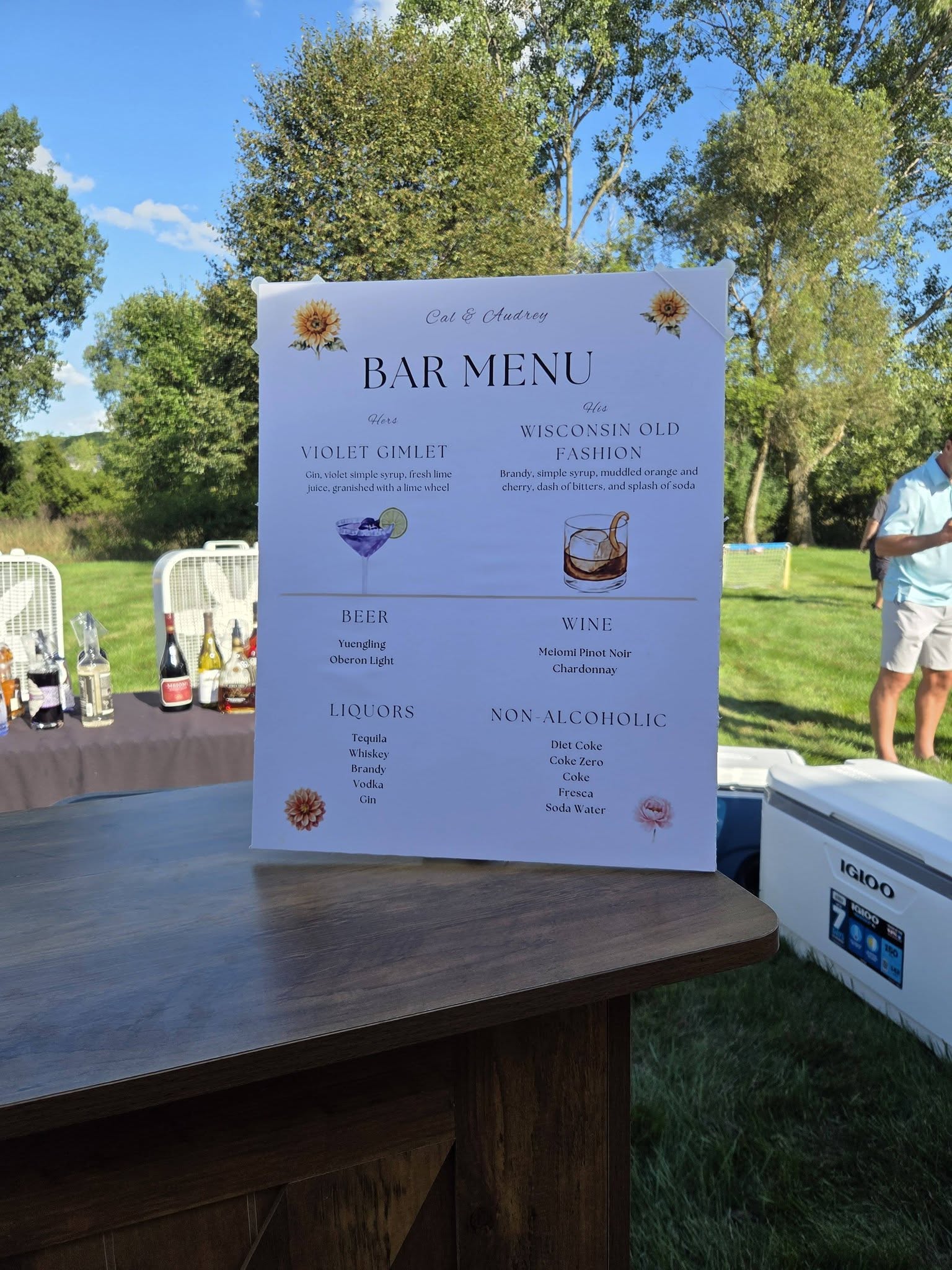A printed bar menu for Cal and Audrey standing on the wooden bar, listing a Violet Gimlet and a Wisconsin Old Fashion